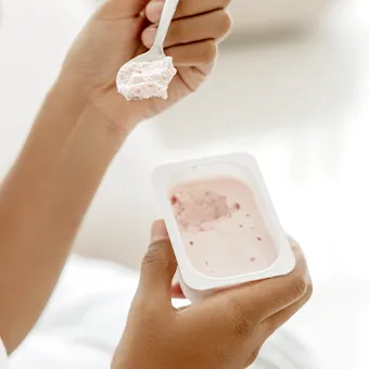 A person lifting a spoonful of pink yoghurt from a small pot