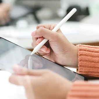 A hand in an orange knitted sleeve writing on a tablet screen with a white stylus