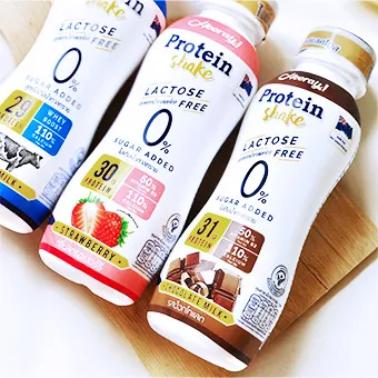 ขวด Hooray Protein Shake 3 ขวด รสนมจืด สตรอว์เบอร์รี และนมช็อกโกแลต วางบนเขียงไม้
