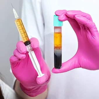 Hands in pink gloves holding a syringe of yellow liquid and a test tube of blood separated into layers