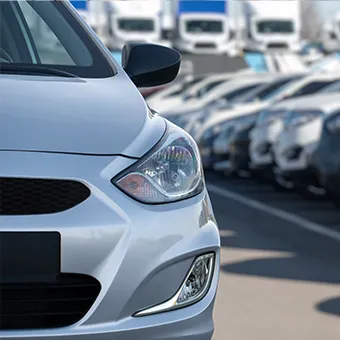 The front of a silver hatchback, with rows of parked cars and white trucks behind it