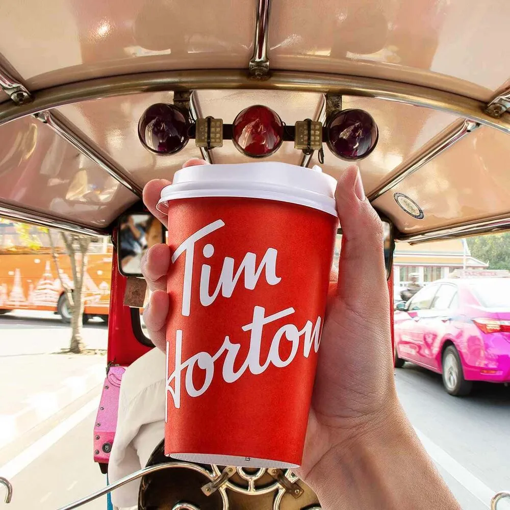 มือถือแก้วกาแฟสีแดงของ Tim Hortons ในรถตุ๊กตุ๊ก ข้างรถแท็กซี่สีชมพูบนถนน
