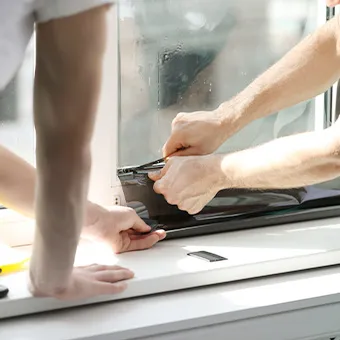 Two pairs of hands pressing dark film onto the lower edge of a window