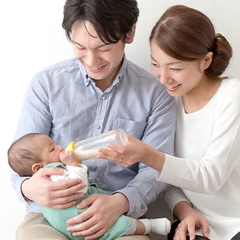 A smiling man holding a baby while a woman feeds it from a bottle