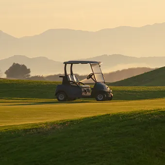 A dark golf cart on a fairway at sunset, with hazy hills behind it