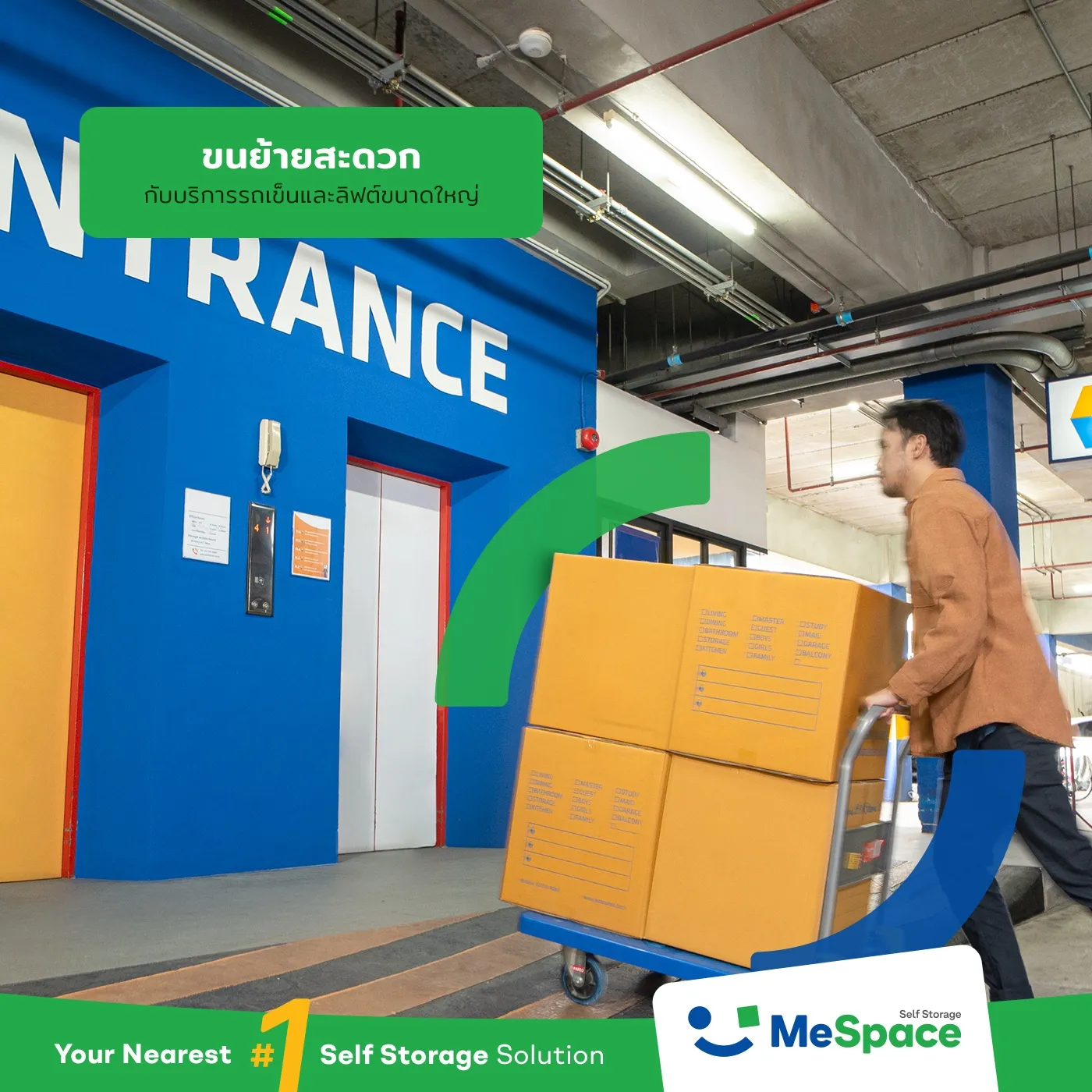 A man pushing a trolley stacked with cardboard boxes past the lifts at a blue entrance wall, under a Thai caption
