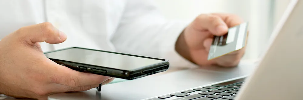 Hands holding a phone and a credit card over a laptop keyboard