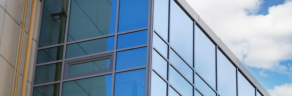 The corner of a glass office building with blue reflective windows against a cloudy sky