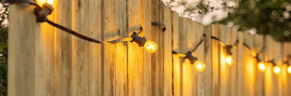 A string of lit bulbs fixed along a wooden fence at dusk
