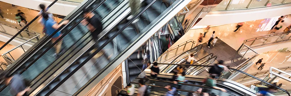 Shoppers on a set of escalators between the floors of a busy shopping centre, blurred by motion