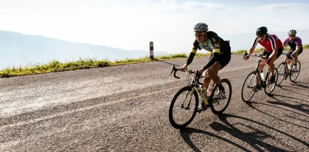Three road cyclists in helmets riding along a mountain road, with a hazy valley behind them