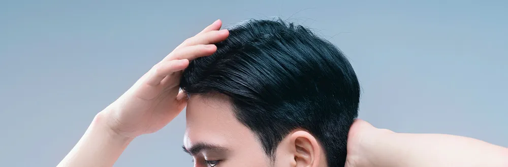 ผู้ชายใช้มือข้างหนึ่งยกผมสีดำด้านหน้าขึ้น เห็นใบหน้าตั้งแต่ระดับดวงตาขึ้นไป