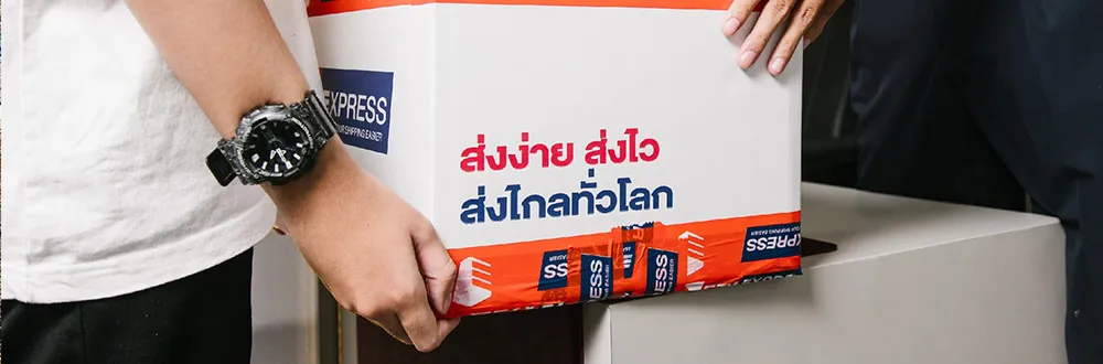 คนสวมเสื้อยืดสีขาวและนาฬิกาสีดำกำลังยกกล่องพัสดุสีขาวของ Ezy Express ที่ปิดด้วยเทปสีส้ม