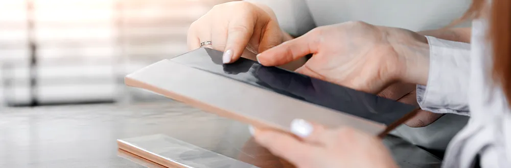 Hands holding a tablet and touching its screen above a desk