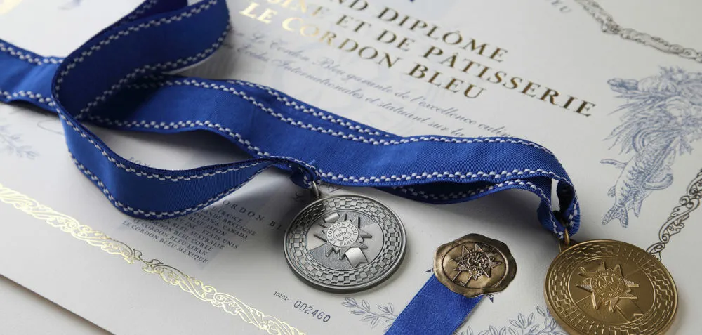 A Le Cordon Bleu Grand Diplôme certificate with a silver medal and a gold medal on blue ribbons