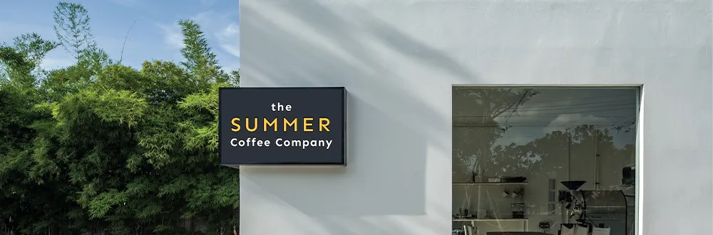 The Summer Coffee Company sign on a white shop wall beside a window, with trees behind